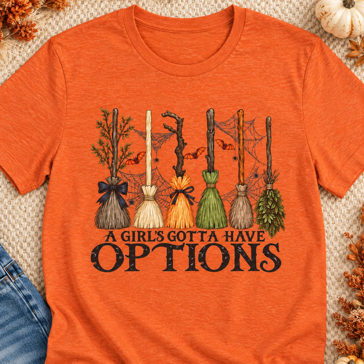 A Girl's Gotta Have Options Witch Brooms T-Shirt — close-up lifestyle flat lay